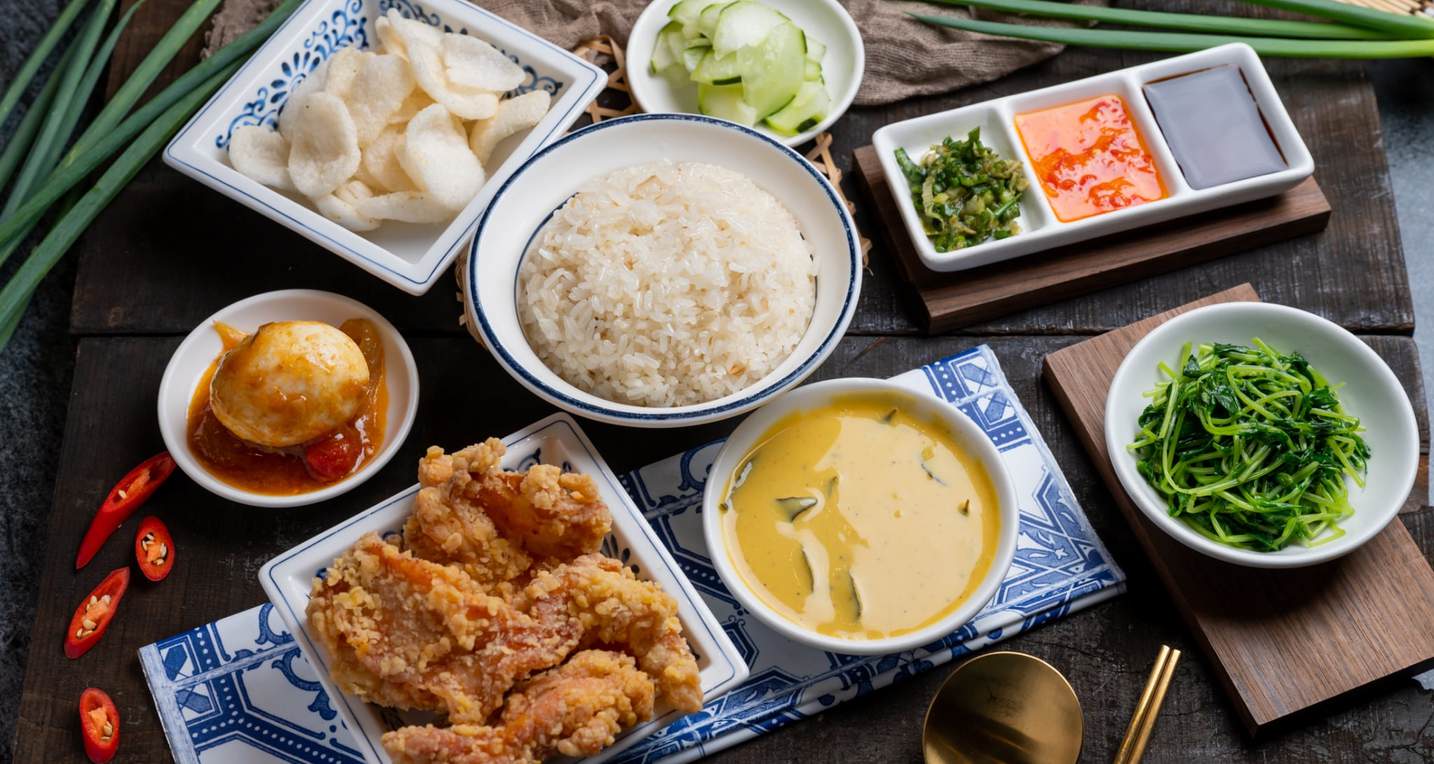 English: Hainanese chicken rice set on wooden table, including rice, fried chicken, curry, vegetables, and dipping sauces. Professional food photography by NiHow Global for Yuan Hainanese Chicken Rice marketing project in London and Taipei. 中文： 海南雞飯套餐擺放在木桌上，包括白飯、炸雞、咖哩、青菜與多種醬料。此為 NiHow Global 專業美食攝影，應用於源海南雞飯於倫敦與台北的行銷專案。